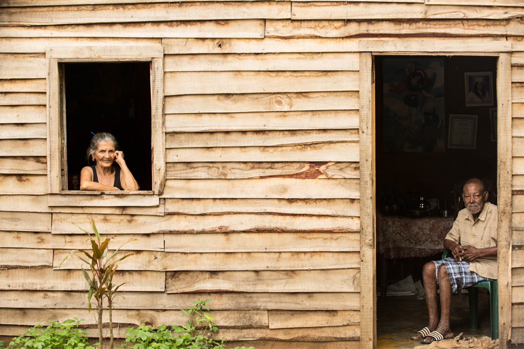 ﻿Woman looking out of window and man sitting in front of doorway in wooden house